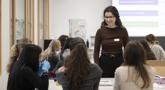 La responsable du module au TecDay se tient devant la classe. Devant elle se trouvent deux rangées d'élèves.
