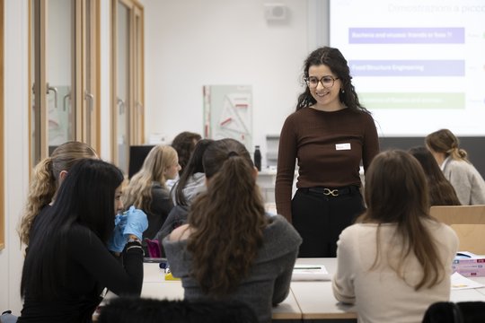 La responsable du module au TecDay se tient devant la classe. Devant elle se trouvent deux rangées d'élèves.