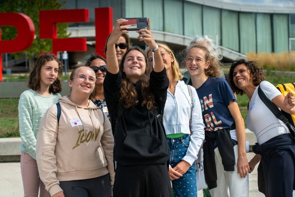 Gruppe von jungen Frauen* im Mentoring macht Selfie vor modernem Gebäude
